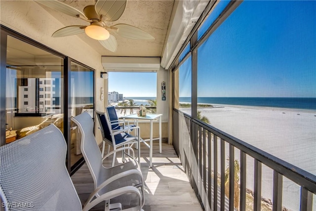 sunroom / solarium featuring ceiling fan, a view of the beach, and a water view