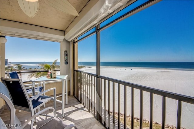 balcony with a view of the beach, a water view, and ceiling fan