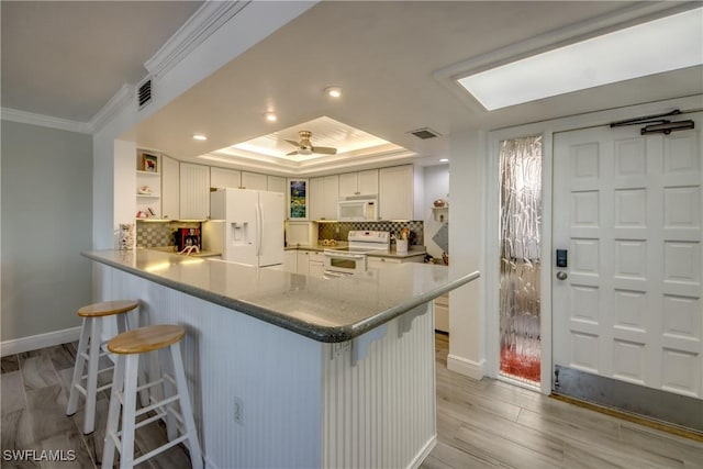 kitchen with a breakfast bar area, kitchen peninsula, white cabinets, and white appliances