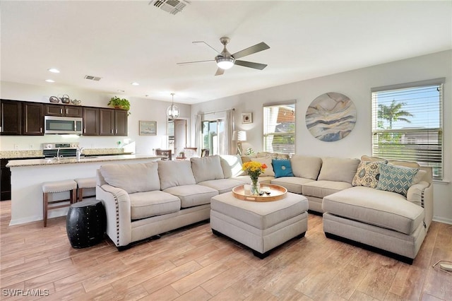 living room with light hardwood / wood-style flooring, ceiling fan with notable chandelier, and sink