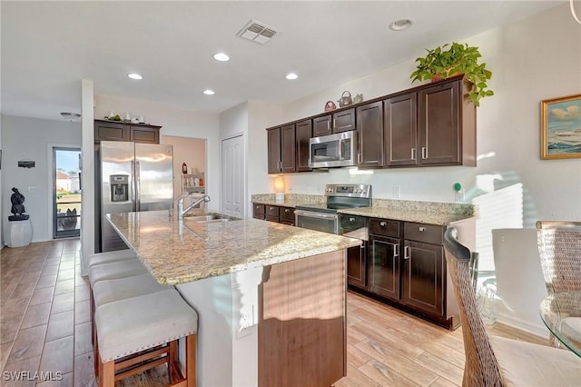 kitchen with an island with sink, sink, appliances with stainless steel finishes, and light hardwood / wood-style flooring