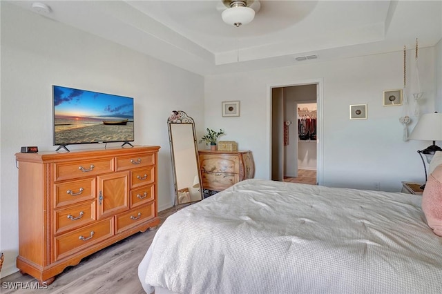 bedroom with ceiling fan, a raised ceiling, and light hardwood / wood-style flooring