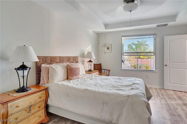 bedroom with light wood-type flooring, a raised ceiling, and ceiling fan