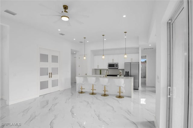 kitchen with pendant lighting, a large island with sink, white cabinets, appliances with stainless steel finishes, and a kitchen bar