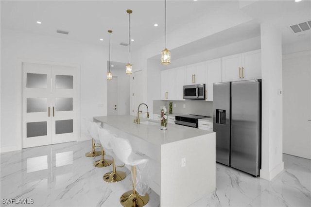 kitchen with white cabinetry, sink, hanging light fixtures, an island with sink, and appliances with stainless steel finishes