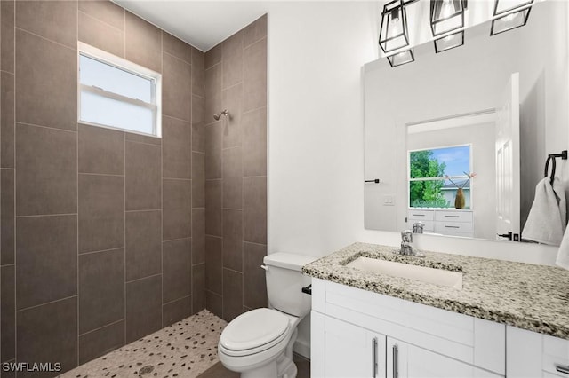 bathroom featuring a tile shower, plenty of natural light, vanity, and toilet