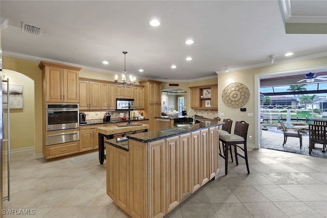 kitchen featuring crown molding, appliances with stainless steel finishes, hanging light fixtures, a kitchen island with sink, and dark stone countertops