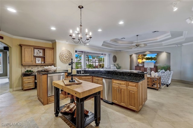 kitchen featuring a tray ceiling, dark stone countertops, stainless steel dishwasher, a center island with sink, and crown molding