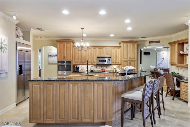 kitchen with sink, stainless steel appliances, backsplash, and an island with sink