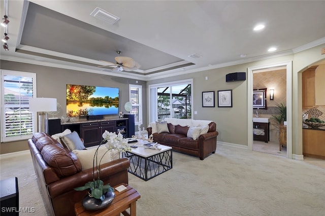 living room featuring light carpet, ornamental molding, and a raised ceiling