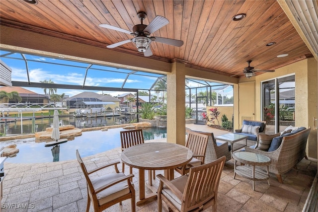 view of patio featuring glass enclosure, ceiling fan, and a water view