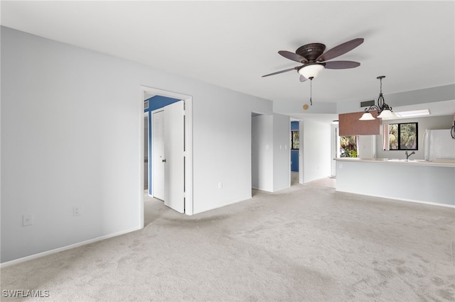 unfurnished living room featuring ceiling fan with notable chandelier, light colored carpet, and sink