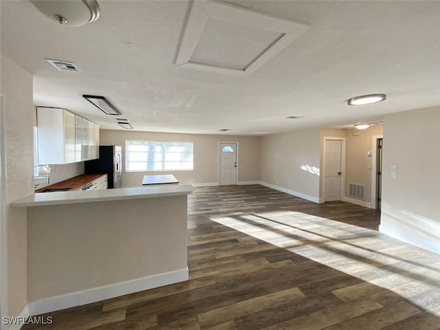 kitchen with dark wood-type flooring, white cabinets, sink, stainless steel fridge, and kitchen peninsula