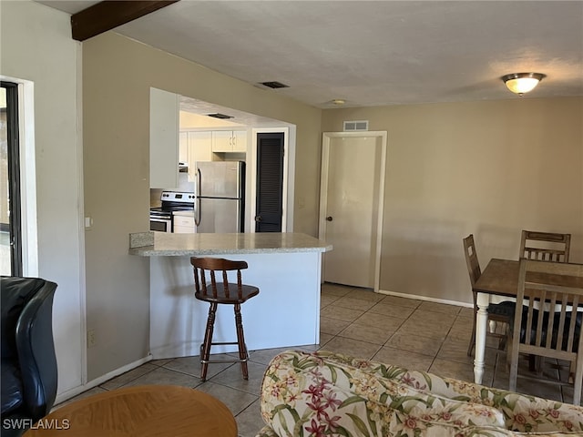 kitchen with kitchen peninsula, electric stove, light tile patterned floors, white cabinets, and stainless steel refrigerator