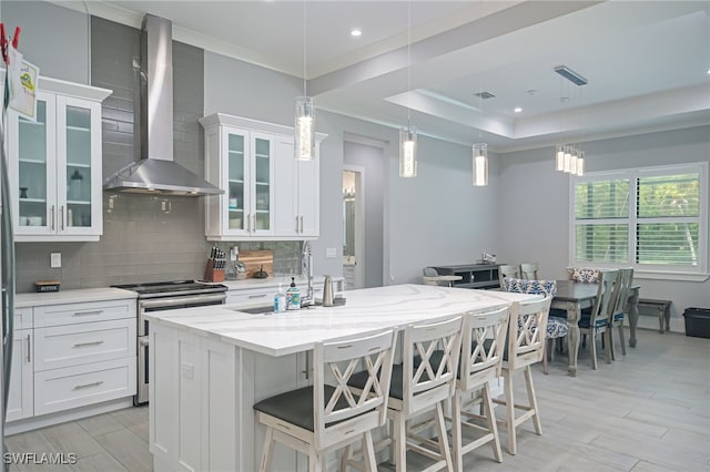 kitchen with light stone countertops, white cabinetry, wall chimney exhaust hood, decorative backsplash, and stainless steel stove