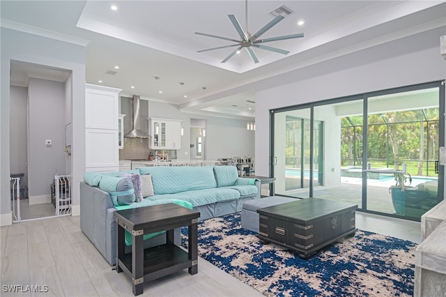 living room with ceiling fan, light wood-type flooring, ornamental molding, and a tray ceiling