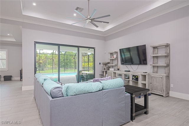 living room with ceiling fan, light wood-type flooring, a high ceiling, and a tray ceiling