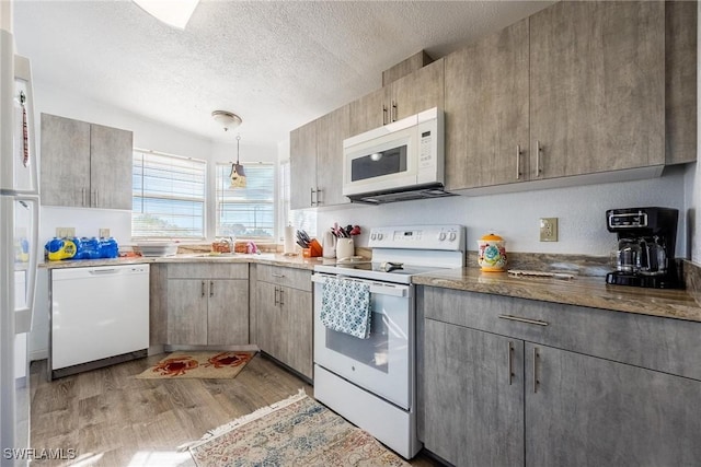 kitchen featuring a textured ceiling, white appliances, sink, pendant lighting, and light hardwood / wood-style floors