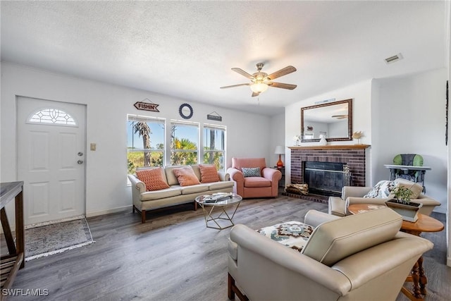 living room with wood-type flooring, a textured ceiling, a brick fireplace, and ceiling fan