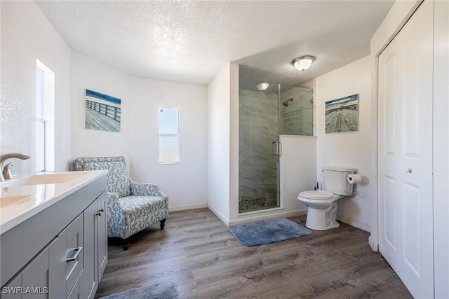 bathroom with hardwood / wood-style floors, a textured ceiling, toilet, vanity, and a shower with shower door