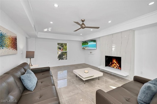 tiled living room with ceiling fan, ornamental molding, a fireplace, and a tray ceiling