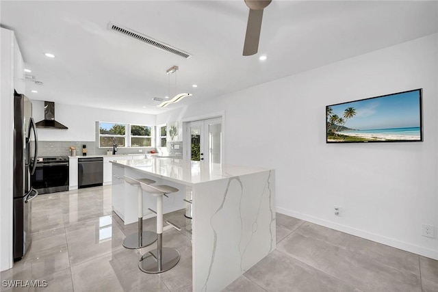 kitchen with white cabinetry, hanging light fixtures, a center island, black appliances, and wall chimney exhaust hood