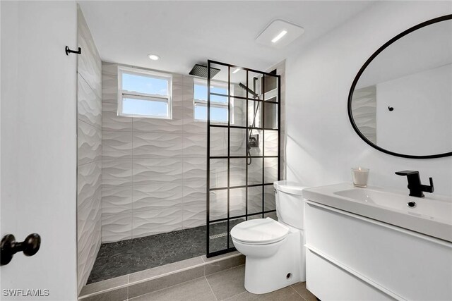 bathroom with a tile shower, tile patterned flooring, vanity, and toilet