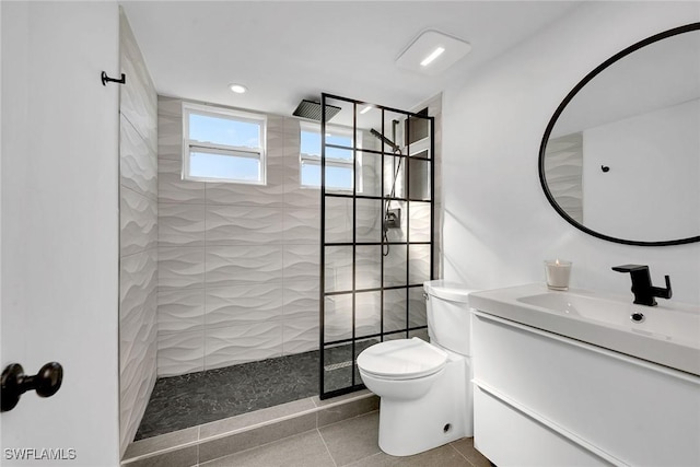 bathroom featuring vanity, a tile shower, tile patterned floors, and toilet