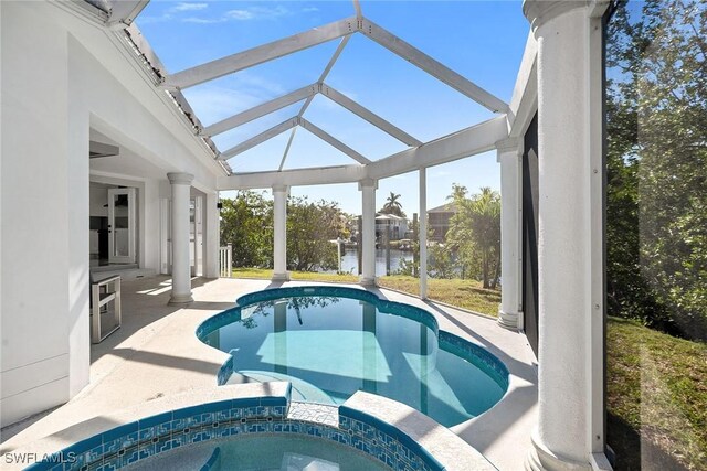 view of pool featuring glass enclosure, a patio area, a water view, and an in ground hot tub