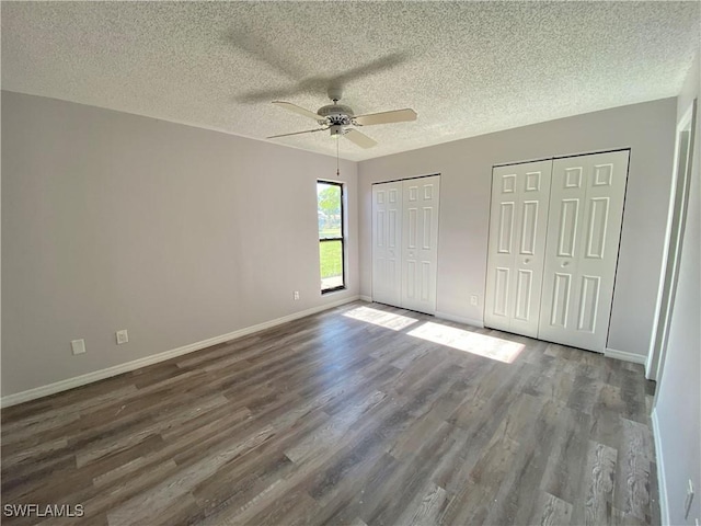 unfurnished bedroom featuring multiple closets, ceiling fan, a textured ceiling, and hardwood / wood-style flooring