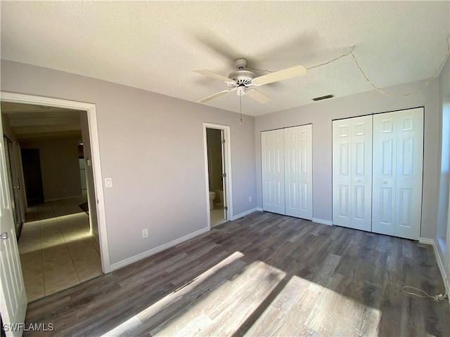 unfurnished bedroom featuring a textured ceiling, ceiling fan, dark wood-type flooring, and multiple closets