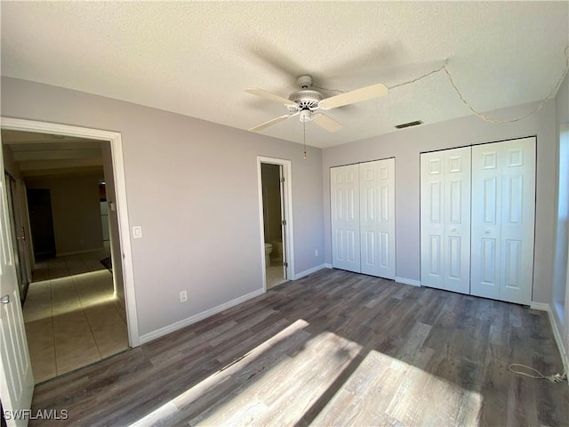 unfurnished bedroom with a textured ceiling, dark hardwood / wood-style flooring, ceiling fan, and multiple closets