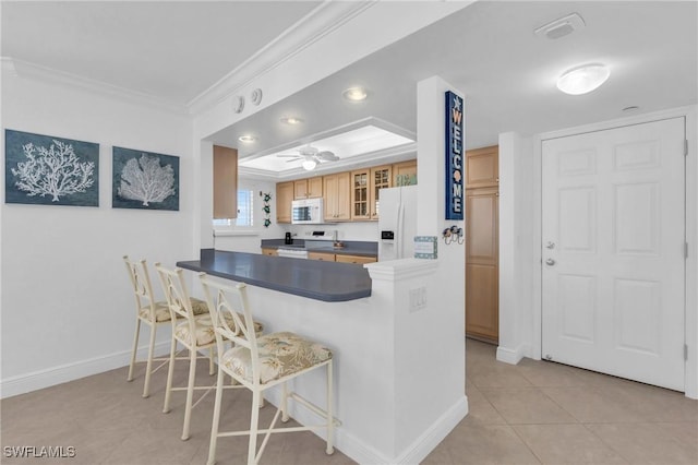 kitchen with dark countertops, glass insert cabinets, white appliances, a peninsula, and a kitchen bar