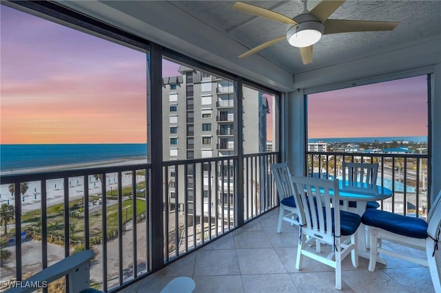 balcony featuring a water view, a view of the beach, and a ceiling fan