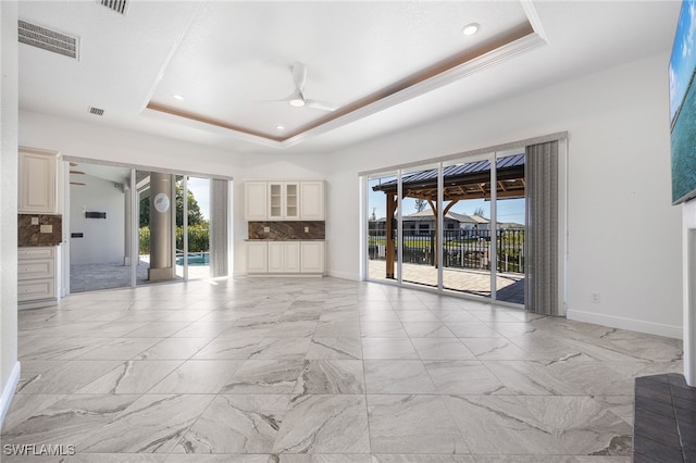 unfurnished living room featuring a tray ceiling, ceiling fan, and plenty of natural light