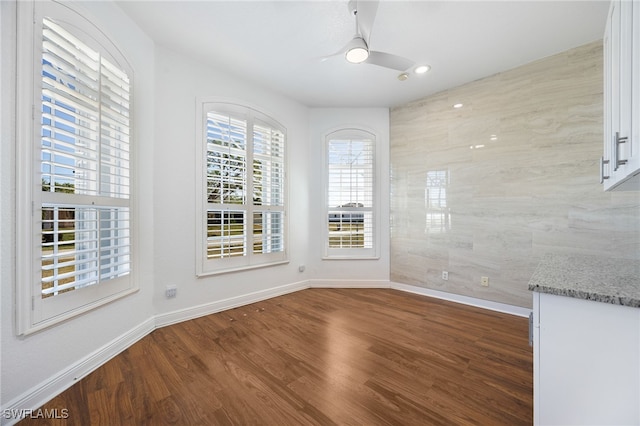 unfurnished dining area featuring hardwood / wood-style flooring, tile walls, and ceiling fan