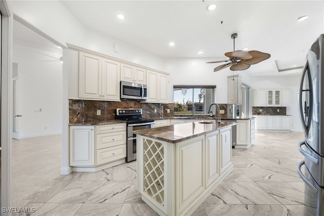 kitchen featuring appliances with stainless steel finishes, backsplash, ceiling fan, white cabinetry, and an island with sink