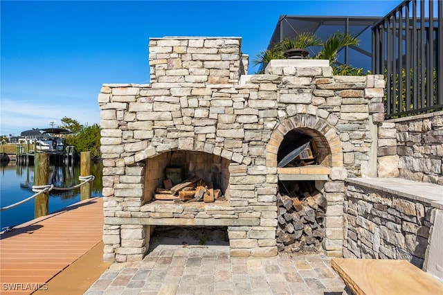 view of patio featuring an outdoor stone fireplace, a water view, and a dock