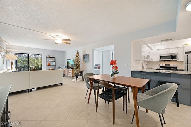 dining room featuring ceiling fan, sink, light tile patterned floors, and a textured ceiling