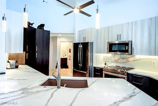 kitchen with pendant lighting, sink, light stone countertops, and stainless steel appliances