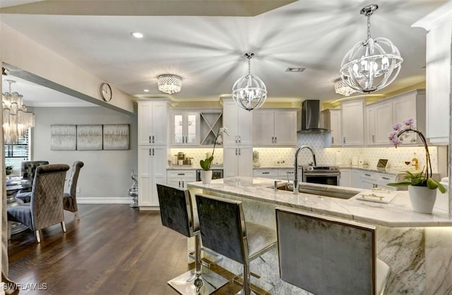 kitchen featuring a breakfast bar, wall chimney range hood, light stone countertops, decorative light fixtures, and dark hardwood / wood-style flooring