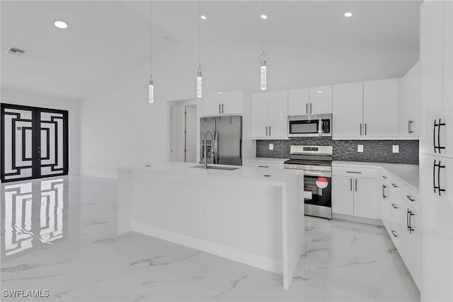 kitchen featuring white cabinets, appliances with stainless steel finishes, decorative light fixtures, and a kitchen island with sink