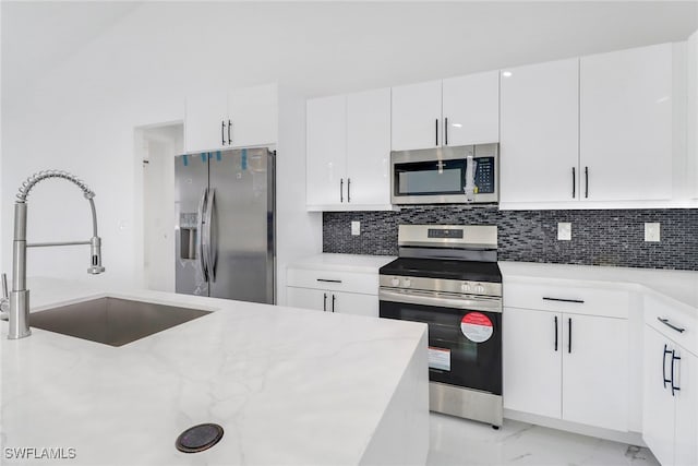 kitchen featuring light stone countertops, sink, stainless steel appliances, decorative backsplash, and white cabinets