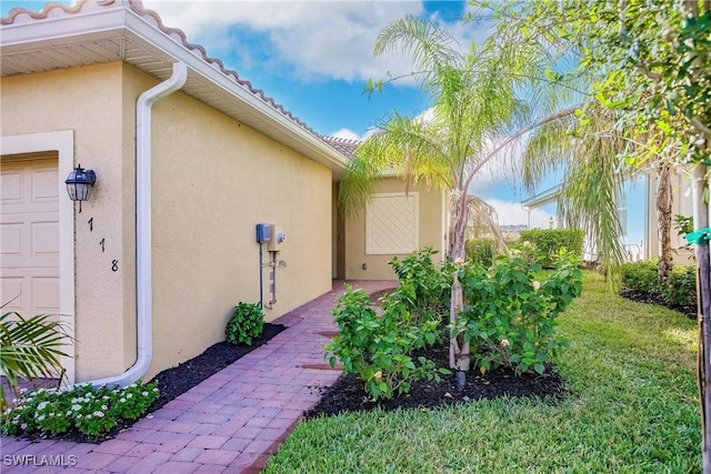 view of exterior entry with stucco siding, a yard, a garage, and a tiled roof