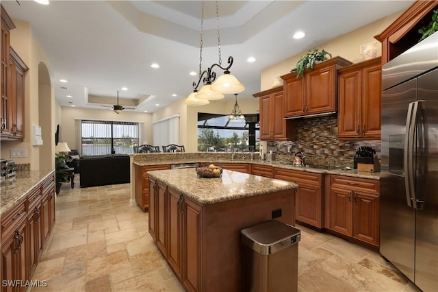 kitchen with built in fridge, a raised ceiling, decorative backsplash, decorative light fixtures, and a kitchen island