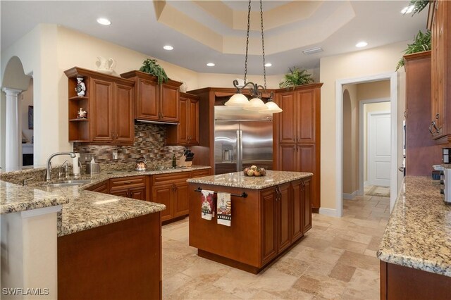 kitchen with backsplash, sink, decorative light fixtures, a kitchen island, and stainless steel built in refrigerator