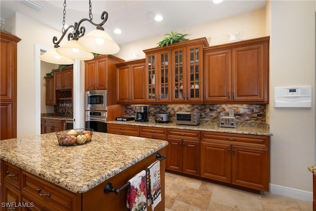 kitchen featuring light stone countertops, decorative backsplash, stainless steel appliances, and decorative light fixtures