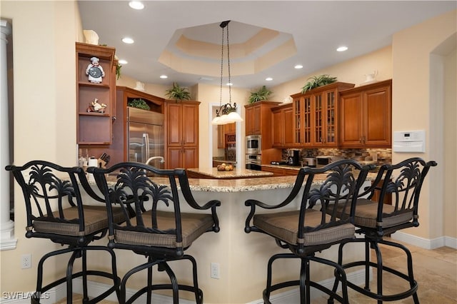 kitchen featuring hanging light fixtures, a raised ceiling, built in appliances, kitchen peninsula, and a breakfast bar area