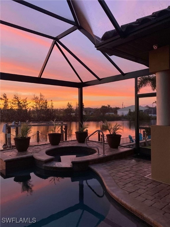 patio terrace at dusk featuring a swimming pool with hot tub, a water view, and a lanai