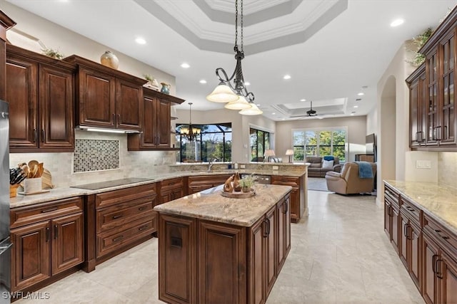 kitchen featuring a center island, black electric stovetop, ceiling fan with notable chandelier, a raised ceiling, and decorative light fixtures